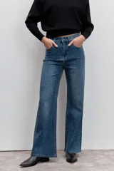 Pantalón de jean corte wide leg, color azul medio, con detalle de strass aplicado en toda la superficie frontal. Cuenta con tiro medio, cierre frontal con botón y bolsillos laterales y traseros.