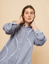 Camisa celeste de algodón con corte oversized, botones frontales a tono y vivos blancos ondulados en el frente.