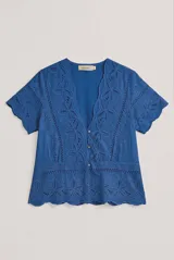 Camisa azul de manga corta confeccionada en tejido broderie con diseño calado y floral. Cuenta con escote en V y cierre frontal de botones.