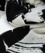 Bufanda confeccionada en franela de acrílico con flecos y estampa de follajes en blanco y negro.