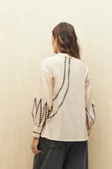 Camisa de lino color beige con bordados geométricos en color negro. Presenta cuello mao, cierre frontal con botones, mangas largas con volumen y puños ajustados.