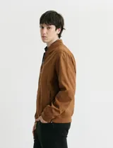 Campera tipo bomber de color marrón, confeccionada en tejido con textura similar a la gamuza, con cierre frontal completo, cuello redondo y puños elásticos.