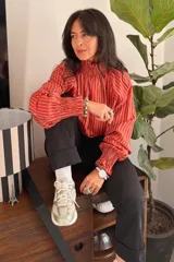 Blusa de tela liviana con diseño de rayas verticales en color terracota y blanco. Presenta cuello alto con detalle de smock, mangas largas con volumen y puños también con detalle de smock.