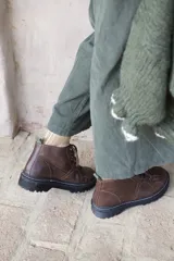 Borcegos de cuero charolado negro con cordones jaspeados en tonos marrones y suela track dentada con costura blanca visible.