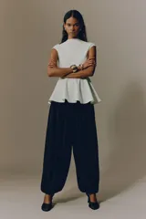 Top en punto roma de color blanco, entallado al cuerpo, con manga japonesa, cuello alto y un delicado peplum con vuelo en la parte inferior.