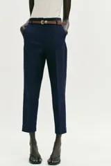 Pantalón tobillero de tiro medio, color azul marino, con bolsillos delanteros y cierre frontal con cremallera, botón y gancho. Incluye un cinturón fino de color marrón con hebilla metálica.