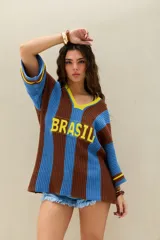Remerón tejido de punto en rayas verticales marrones y celestes, con cuello en V amarillo, mangas 3/4 y la inscripción 'BRASIL' en el frente.