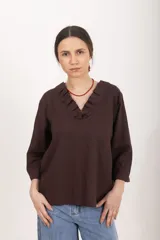 Blusa marrón de lino y viscosa con escote en V y cuello adornado con volados plisados, mangas tres cuartos y corte recto.