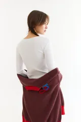 Top de manga larga color blanco, confeccionado en tejido de punto acanalado con diseño irregular y aberturas para los pulgares en los puños.