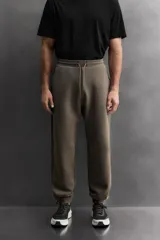 Pantalón jogger de entrenamiento, corte regular fit, color verde oliva oscuro. Confeccionado en tejido técnico compacto de algodón con elasticidad y efecto neopreno. Presenta cintura elástica ajustable con cordón blanco, bolsillos frontales y un bolsillo lateral con cierre de cremallera. El bajo termina en puño.