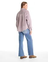 Sobrecamisa de pana con textura acanalada, corte oversize y silueta holgada. Presenta cuello clásico, cierre frontal con botones metálicos, mangas largas con puños abotonados y dos bolsillos frontales tipo parche con solapa.