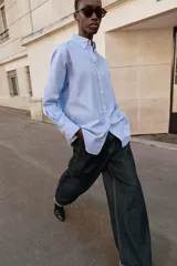 Camisa de corte oversize con cuello solapa, manga larga con puños y bajo asimétrico. Cierre frontal con botones.