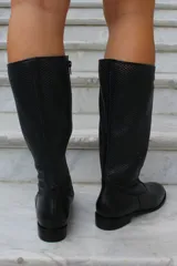 Bota de caña alta confeccionada en cuero, con diseño de textura perforada en la parte superior de la caña y puntera lisa. Cuenta con suela plana y taco bajo.