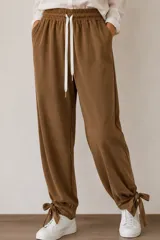 Pantalón de viscosa y algodón color marrón, de corte holgado estilo aladino, con cintura elastizada, cordón ajustable blanco y lazos para atar en los tobillos.