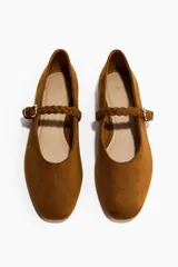 Ballerinas de gamuza color marrón con punta redondeada y tira trenzada ajustable en el empeine con hebilla metálica.