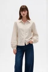 Camisa de algodón a rayas finas en tonos beige y blanco, de corte entallado, con cuello camisero, cierre frontal de botones y mangas largas abullonadas con puños ajustados.