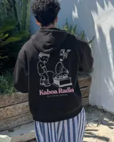Canguro negro con capucha, de corte regular y confección en felpa suave, con estampa en la espalda de un personaje gráfico y texto "Kaboa Radio".