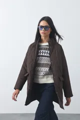 Campera capitoneada de largo medio en color marrón, con cuello alto, cierre frontal y broches a presión. Cuenta con bolsillos laterales con solapa y diseño acolchado con costuras en forma de rombos.