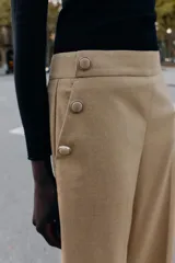 Pantalón tipo culotte de tiro alto, con pernera ancha y corta. Presenta detalles de botones dorados decorativos en la parte frontal y cierre lateral con cremallera oculta.
