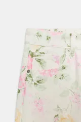 Jeans de tiro bajo y corte suelto con diseño de cinco bolsillos, trabillas para cinto y cierre frontal con cremallera y botón metálico, adornado con un estampado floral en tonos rosados y verdes sobre base clara.