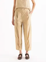 Pantalón slouchy de poplín color beige, de calce regular y largo al tobillo, con tablas en el delantero y ruedo que aportan volumen, bolsillos laterales y cierre con botones tipo honguito.