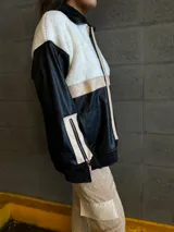 Campera con cuerpo de corderito color beige, mangas y parte inferior de cuero sintético negro con textura tipo cocodrilo. Tiene cuello estilo camisa con solapas de corderito negro, cierre frontal con cremallera y bolsillos laterales.