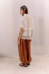 Camisa de algodón color crudo, con cuello camisero, mangas cortas y cierre frontal con botones. Presenta paneles de tejido calado y detalles bordados transparentes.