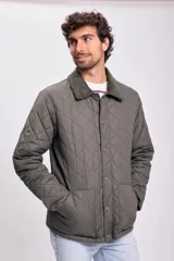 Campera capitonada de color verde oliva, con cierre frontal mediante botones a presión y cuello de pana en tono contrastante. Presenta un diseño acolchado con patrón de rombos y bolsillos laterales.