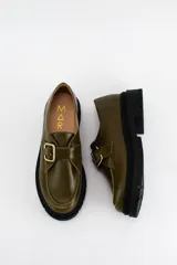 Mocasines de cuero color verde oliva con suela track negra de plataforma. Presentan una tira decorativa sobre el empeine con hebilla metálica dorada ajustable en el lateral.