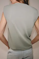 Top de punto negro con cuello redondo, manga sisa, hombreras y detalle de pliegues en la parte delantera.
