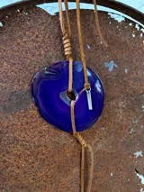 Collar con dije de piedra ágata blanca y marrón, con forma circular irregular y agujero en el centro. El dije está sujeto con un cordón fino de cuero marrón.