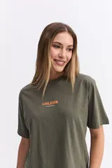 Remera de algodón color verde oliva, con corte relajado y manga corta. Presenta una estampa gráfica grande en la espalda con motivos florales abstractos y texto.