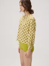 Camisa voluminosa de algodón con mangas amplias y abullonadas que se ajustan en los puños. Tiene calce suelto, hombro caído, cuello redondo y cierre frontal con botones. Presenta estampado geométrico en tonos mostaza y beige.