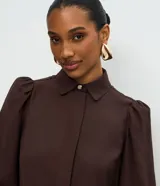 Camisa de crepé color celeste, con cuello inglés, manga larga abullonada y cierre frontal oculto con botón diferenciado en el cuello.