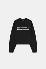 Sudadera negra de cuello redondo y manga larga, con texto blanco "SCREENWRITER & MAIN CHARACTER" en el delantero. Acabados en rib a tono.