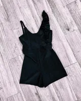 Mono corto blanco con escote en V, breteles finos y un volado en el hombro izquierdo.