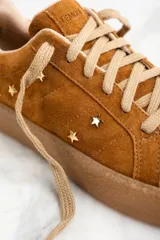 Zapatillas bajas de gamuza color marrón con apliques de estrellas doradas.