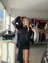 Vestido corto negro de mangas largas acampanadas y cuello redondo. Presenta un diseño ajustado con un detalle de nudo frontal que cae en forma de lazo, creando un efecto asimétrico.