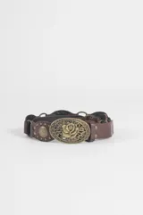 Cinturón marrón de cuero vegano con hebilla ovalada de metal dorado envejecido con relieve de flor y detalles de tachas y aros metálicos.
