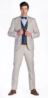 Ambo de tres piezas compuesto por saco, pantalón y chaleco. El saco y el pantalón son de color beige, mientras que el chaleco presenta un diseño estampado en tonos azul oscuro. Incluye camisa clara y moño a juego.