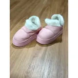 Pantuflas botitas color tostado con diseño acolchado y plataforma, forradas con corderito sintético blanco en el interior y el cuello. Cuentan con una pequeña etiqueta decorativa en el lateral.