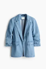 Blazer de denim de algodón celeste, con solapas de muesca, hombreras y mangas tres cuartos fruncidas. Cuenta con bolsillos delanteros con solapa y diseño abierto sin cierre.