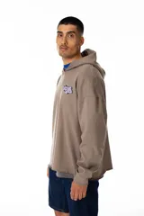 Buzo con capucha color marrón topo, de corte oversize y terminación sin franja en la cintura. Presenta un estampado pequeño en el pecho con el logo de la marca en color lila.