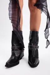 Bota de caña media confeccionada en cuero vacuno negro, con diseño de estilo western. Presenta una puntera estilizada, taco bajo y una correa decorativa con tachas metálicas y hebilla plateada que rodea el tobillo.