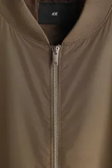 Campera bomber liviana H&M de color verde militar, con cuello, puños y dobladillo acanalados. Cuenta con cierre frontal plateado, bolsillos laterales con solapa y diseño clásico de aviador.