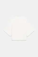 Top blanco de tejido rústico, con cuello redondo y mangas cortas amplias. Bajo recto.