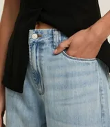 Pantalón de jean de corte wide leg, tiro alto, con bolsillos delanteros y traseros, trabillas para cinturón y cierre frontal con cremallera y botón.