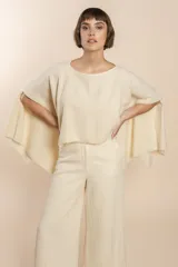 Poncho color beige con diseño a cuadros, cuello bote y terminaciones desflecadas. Tiene aberturas para los brazos en los laterales y detalles en cuero.