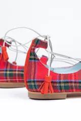 Bailarinas rojas con estampado tartán, anudadas al tobillo con cordones blancos y borlas decorativas.