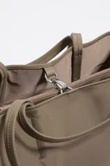 Bolso shopper de gran capacidad confeccionado en nylon color marrón, con estructura blanda, doble asa de mano y logo metálico de la marca en la parte frontal. Incluye cierre con mosquetón y bolsillo interior.